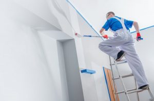 A worker painting a wall on a ladder.