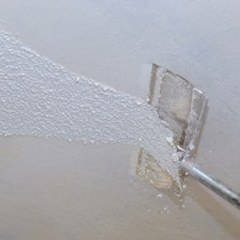 person using tool to remove popcorn ceiling