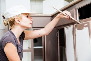 A woman painting kitchen cabinets.