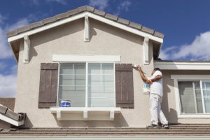 A man standing on a roof painting a house.