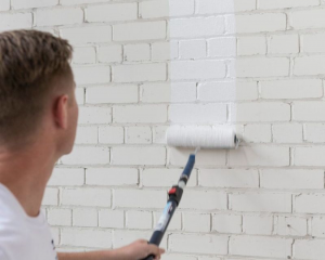 a person painting an exterior brick wall